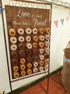 Donut wall in a marquee, a mix of chocolate, plain and pink donuts on a peg board with a copper pipe frame