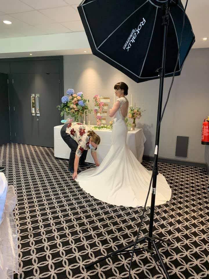 Your Wedding Friend helping a photographer set up a shot readying a brides dress at her cake table