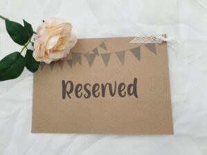 A rustic card has the word reserved printed on it with a cream rose  placed on it at the top left