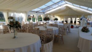 marquee with round tables and chairs laid out for a reception